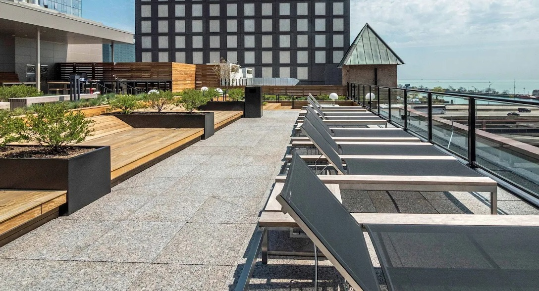 Sunny rooftop patio with lounge chairs, wooden decking, and views of the lake and city skyline at Lofts at River East in Chicago