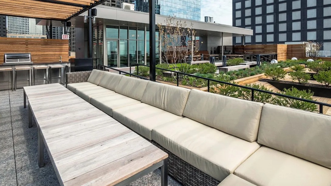Spacious rooftop lounge with comfortable sectional sofas, outdoor dining tables, and a grilling station under a stylish pergola at Lofts at River East in Chicago
