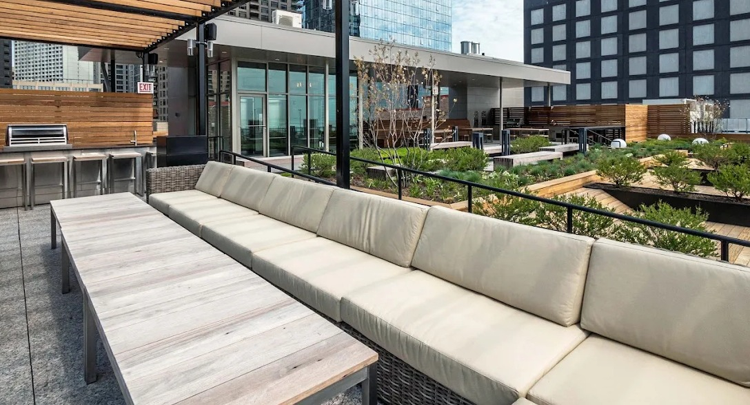 Spacious rooftop lounge with comfortable sectional sofas, outdoor dining tables, and a grilling station under a stylish pergola at Lofts at River East in Chicago