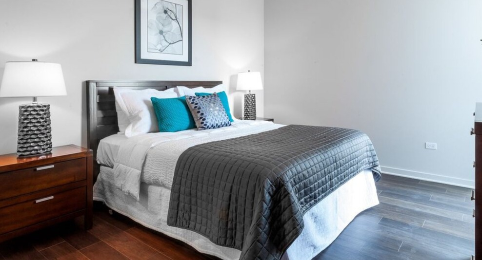 A tranquil bedroom at Luxe on Chicago Apartments, featuring a queen-sized bed, dark hardwood floors, and modern decor