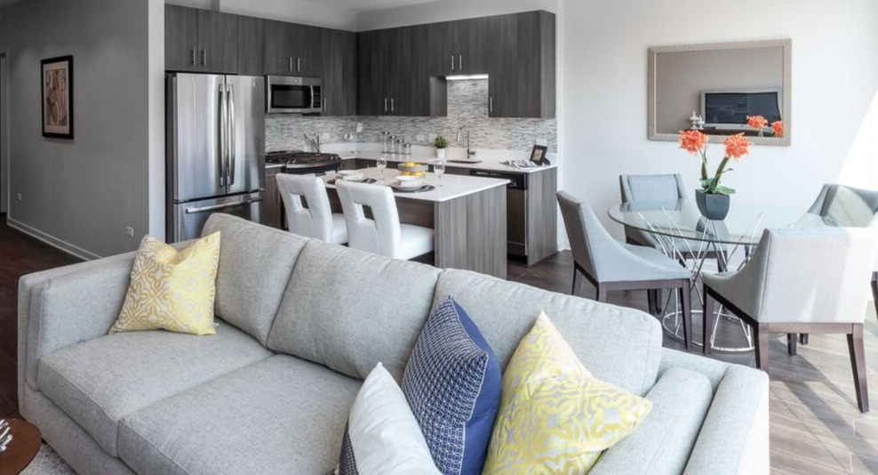 A sun-filled living and dining area at Luxe on Chicago Apartments, with modern furniture and a view of the city