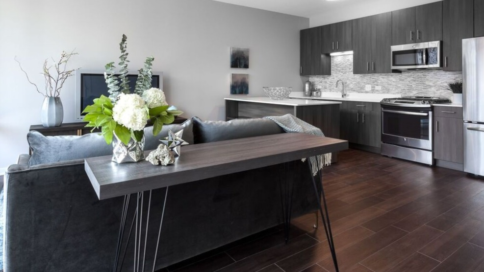 A wide shot of the contemporary kitchen and living room at Luxe on Chicago Apartments, featuring dark wood floors