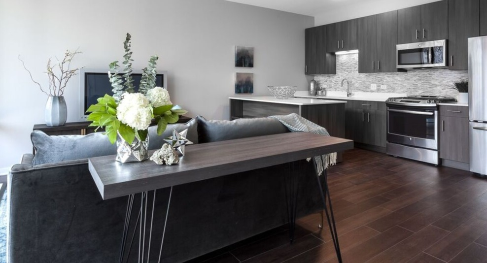 A wide shot of the contemporary kitchen and living room at Luxe on Chicago Apartments, featuring dark wood floors