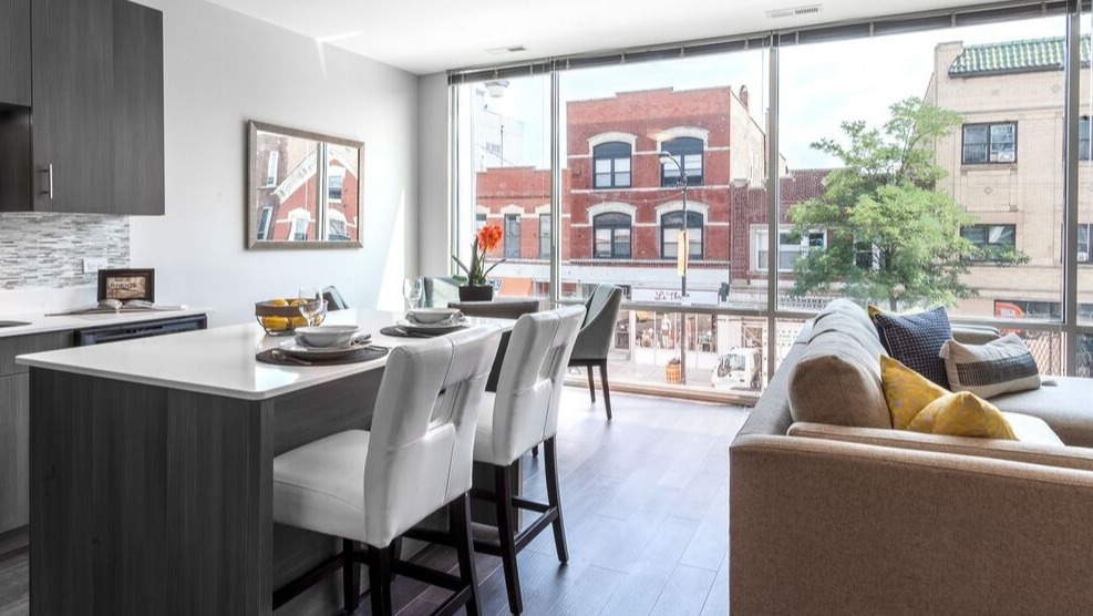 A modern kitchen and living area at Luxe on Chicago Apartments, with floor-to-ceiling windows overlooking city buildings