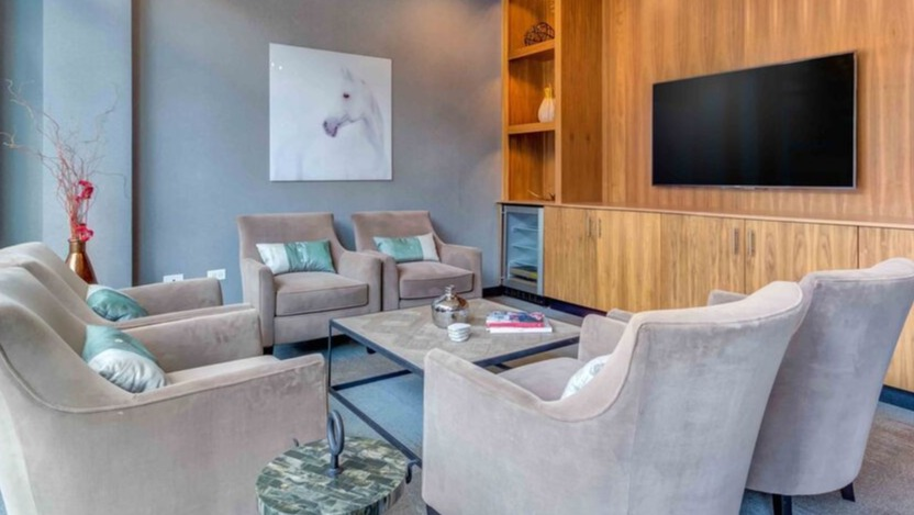A cozy resident lounge at Luxe on Chicago Apartments, featuring comfortable armchairs, a large TV, and elegant wood accents
