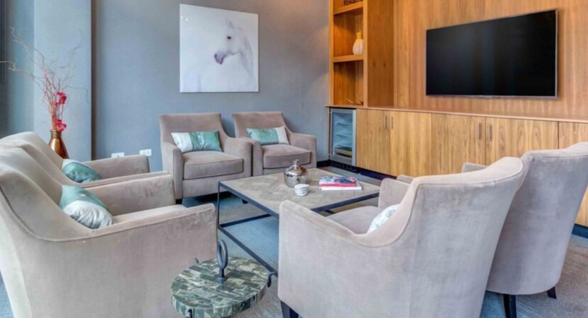 A cozy resident lounge at Luxe on Chicago Apartments, featuring comfortable armchairs, a large TV, and elegant wood accents