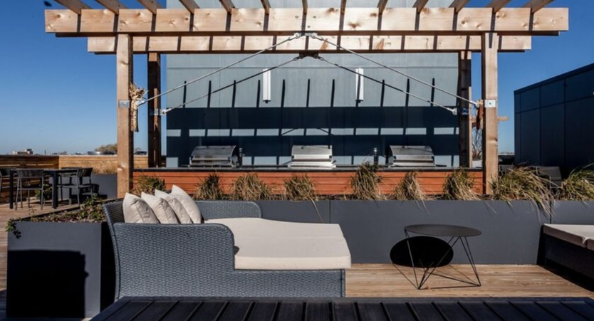 A sunny rooftop deck at Luxe on Chicago Apartments with outdoor grills, lounge seating, and pergolas