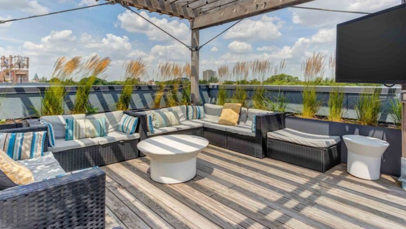 A stylish rooftop lounge at Luxe on Chicago Apartments with abundant seating, an outdoor TV, and string lights under a pergola