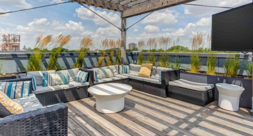 A stylish rooftop lounge at Luxe on Chicago Apartments with abundant seating, an outdoor TV, and string lights under a pergola