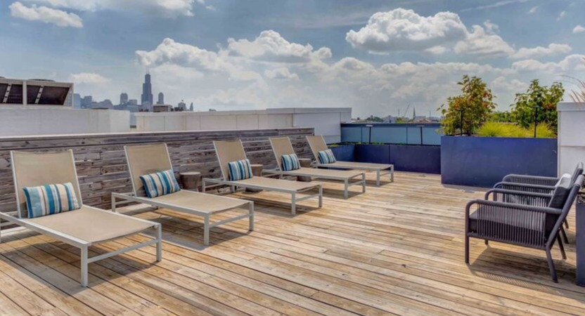 A spacious rooftop sun deck at Luxe on Chicago Apartments with comfortable lounge chairs and a distant city skyline