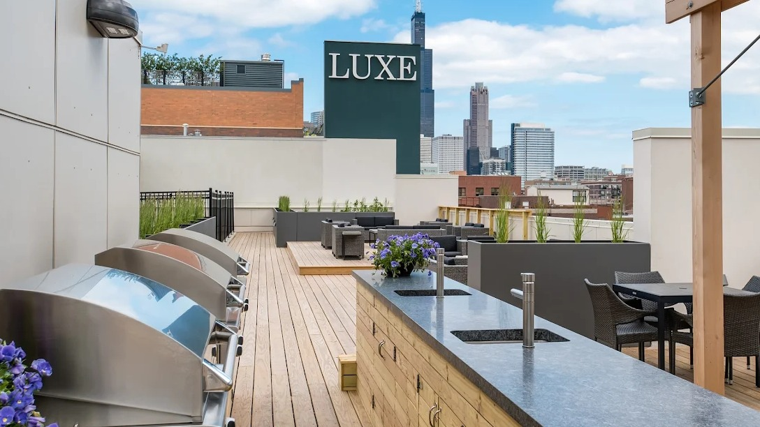 Rooftop amenity space with outdoor kitchens, grilling stations, dining areas, and Chicago skyline views at Luxe on Madison Apartments