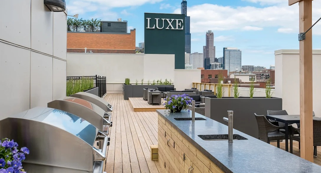 Rooftop amenity space with outdoor kitchens, grilling stations, dining areas, and Chicago skyline views at Luxe on Madison Apartments