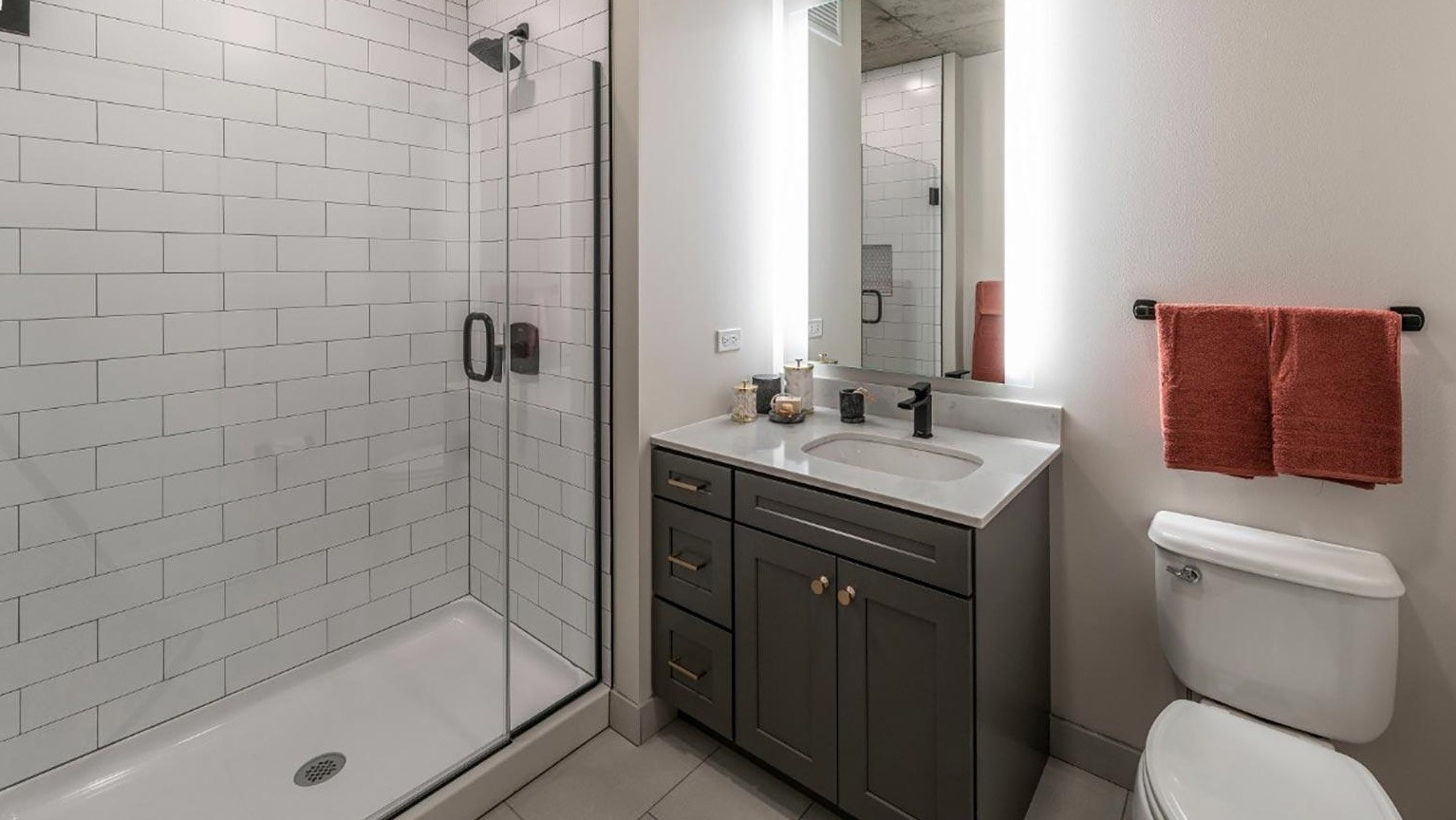 Contemporary bathroom featuring a glass-enclosed shower with subway tiles, a modern vanity, and illuminated mirror at Marlowe Apartments in Chicago