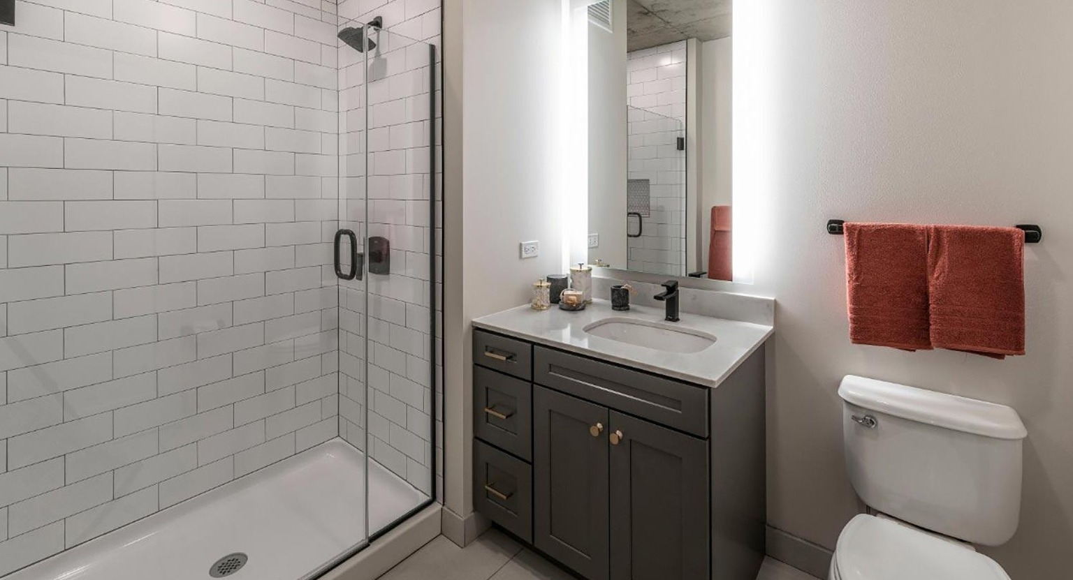 Contemporary bathroom featuring a glass-enclosed shower with subway tiles, a modern vanity, and illuminated mirror at Marlowe Apartments in Chicago