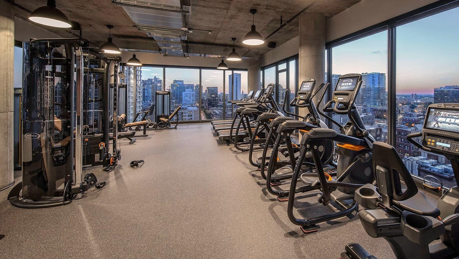 State-of-the-art fitness center with a range of cardio machines, strength equipment, and large windows overlooking the city at Marlowe Apartments in Chicago