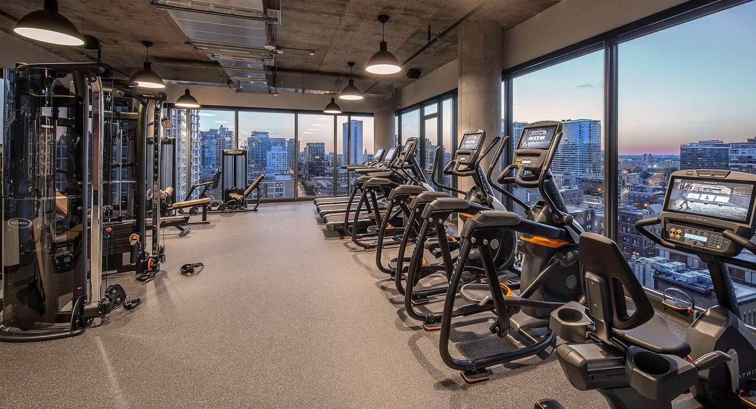 State-of-the-art fitness center with a range of cardio machines, strength equipment, and large windows overlooking the city at Marlowe Apartments in Chicago