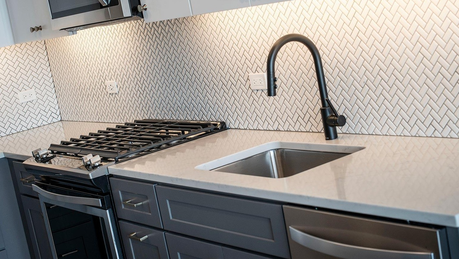 Detailed view of a modern kitchen with a herringbone tile backsplash, gas range, stainless steel sink, and sleek cabinetry at Marlowe Apartments in Chicago