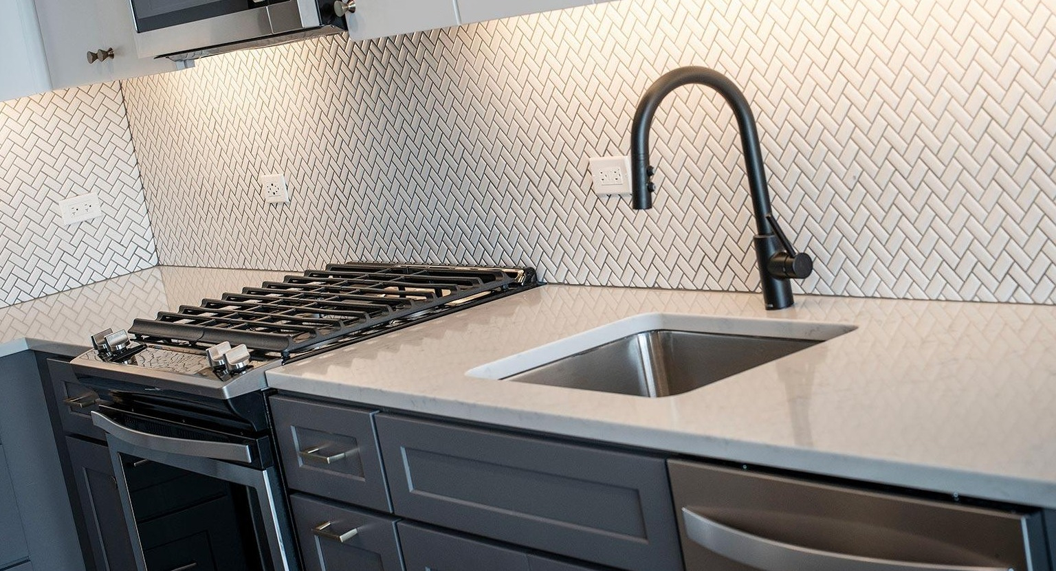 Detailed view of a modern kitchen with a herringbone tile backsplash, gas range, stainless steel sink, and sleek cabinetry at Marlowe Apartments in Chicago