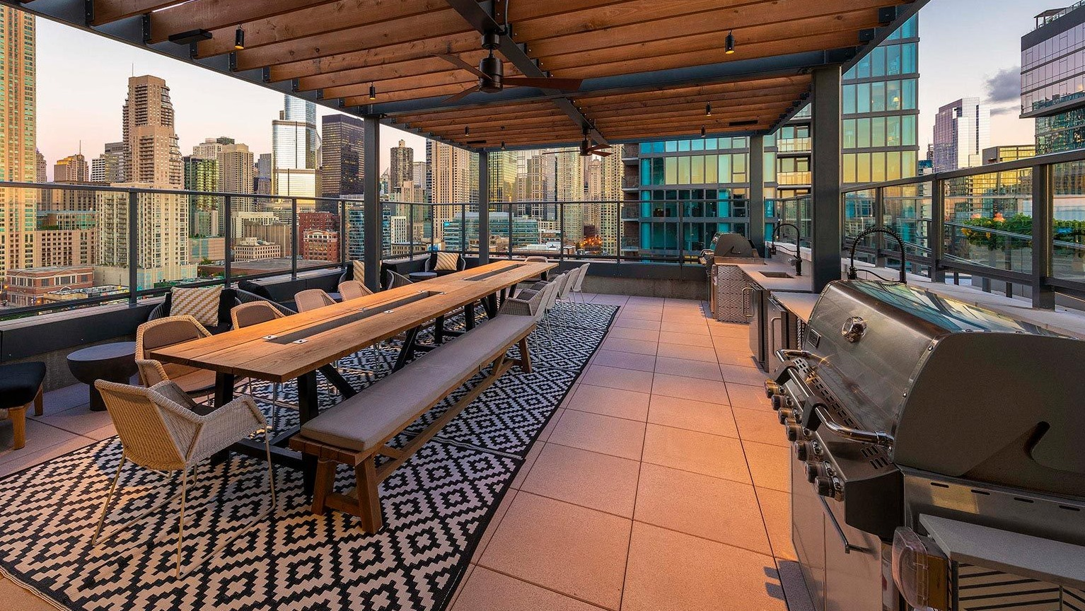 Expansive rooftop terrace with a large communal dining table, grilling stations, and stunning panoramic city views at Marlowe Apartments in Chicago