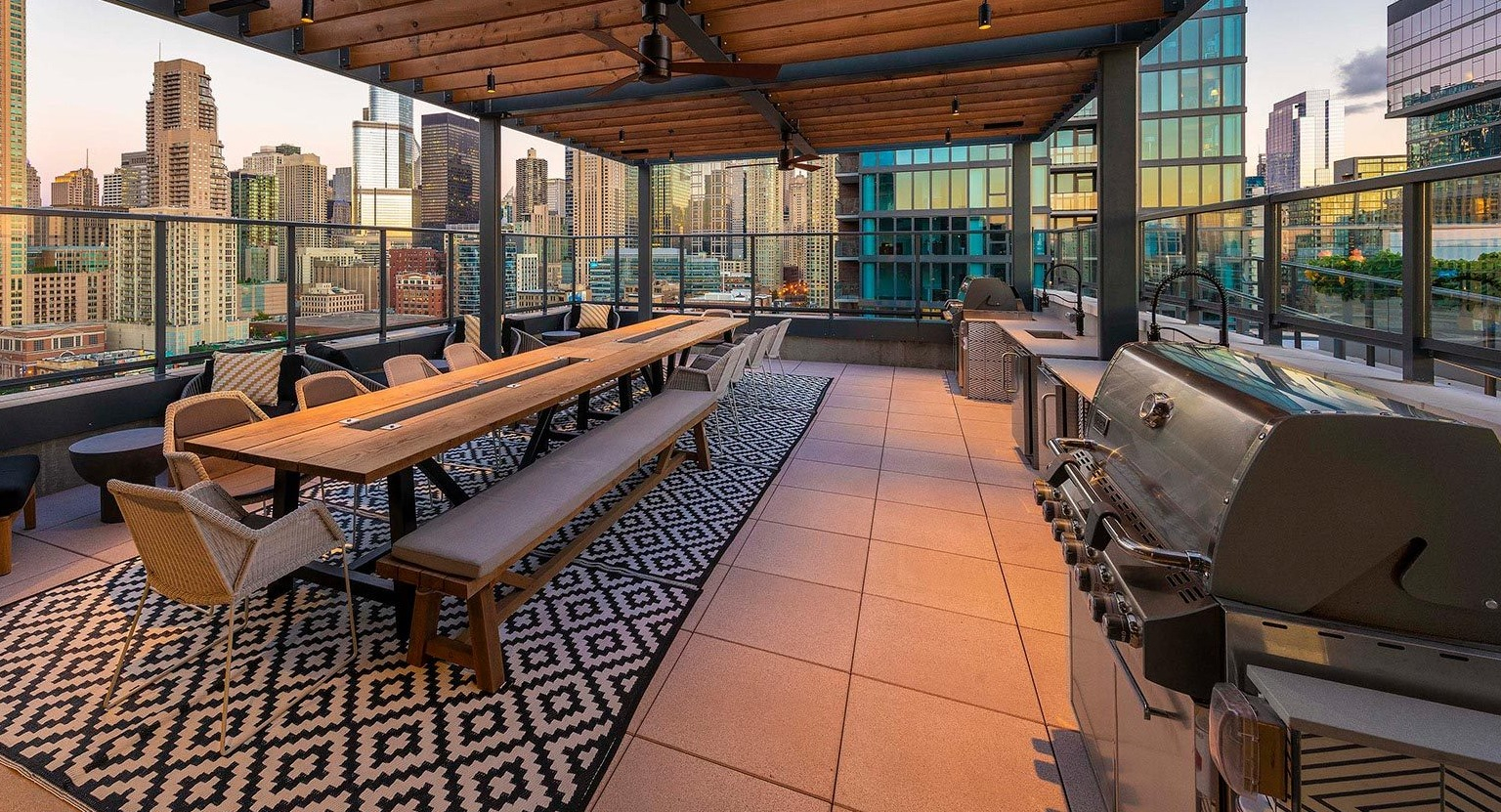 Expansive rooftop terrace with a large communal dining table, grilling stations, and stunning panoramic city views at Marlowe Apartments in Chicago