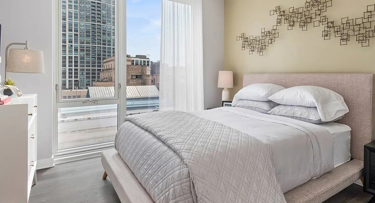 Bright and cozy bedroom with a comfortable bed, modern decor, and large windows offering city views at Marquee at Block 37 in Chicago