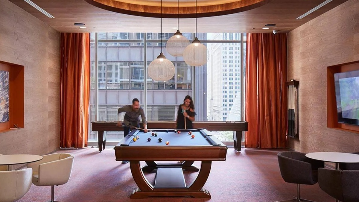 Residents enjoying a game of billiards in the modern game room with large windows at Marquee at Block 37 apartments in Chicago