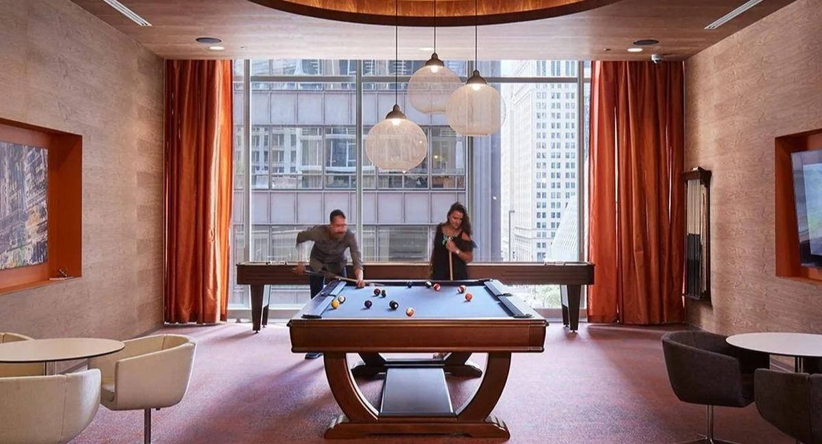 Residents enjoying a game of billiards in the modern game room with large windows at Marquee at Block 37 apartments in Chicago