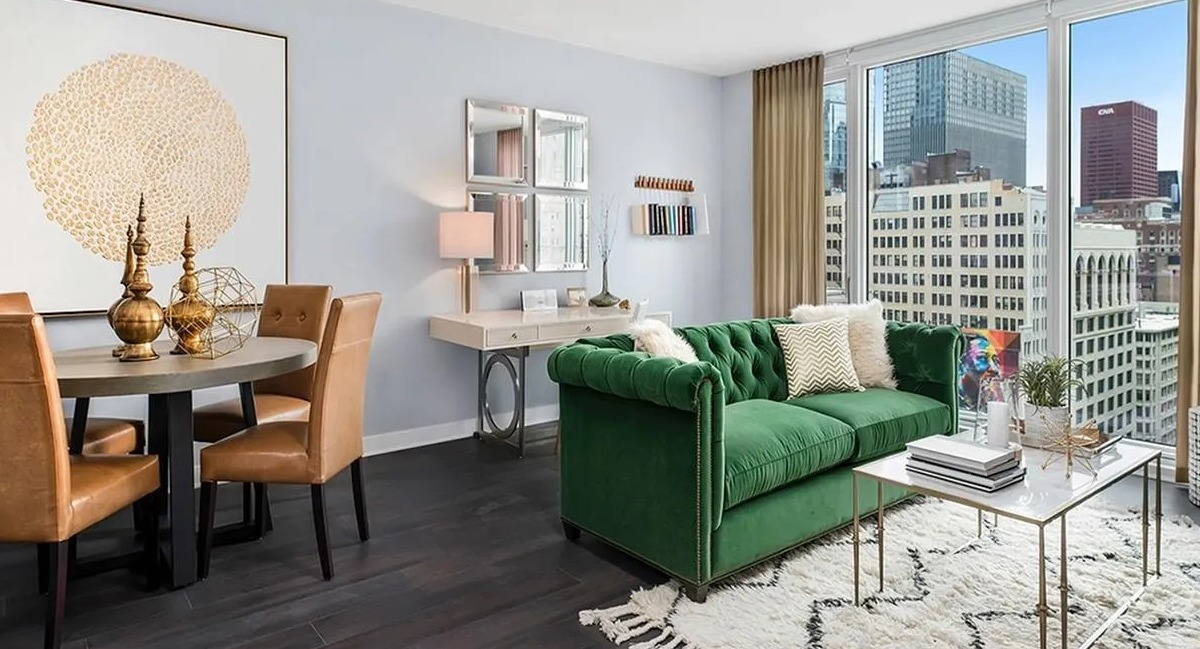Modern living and dining area with a green sofa, stylish rug, and city views from large windows at Marquee at Block 37 in Chicago