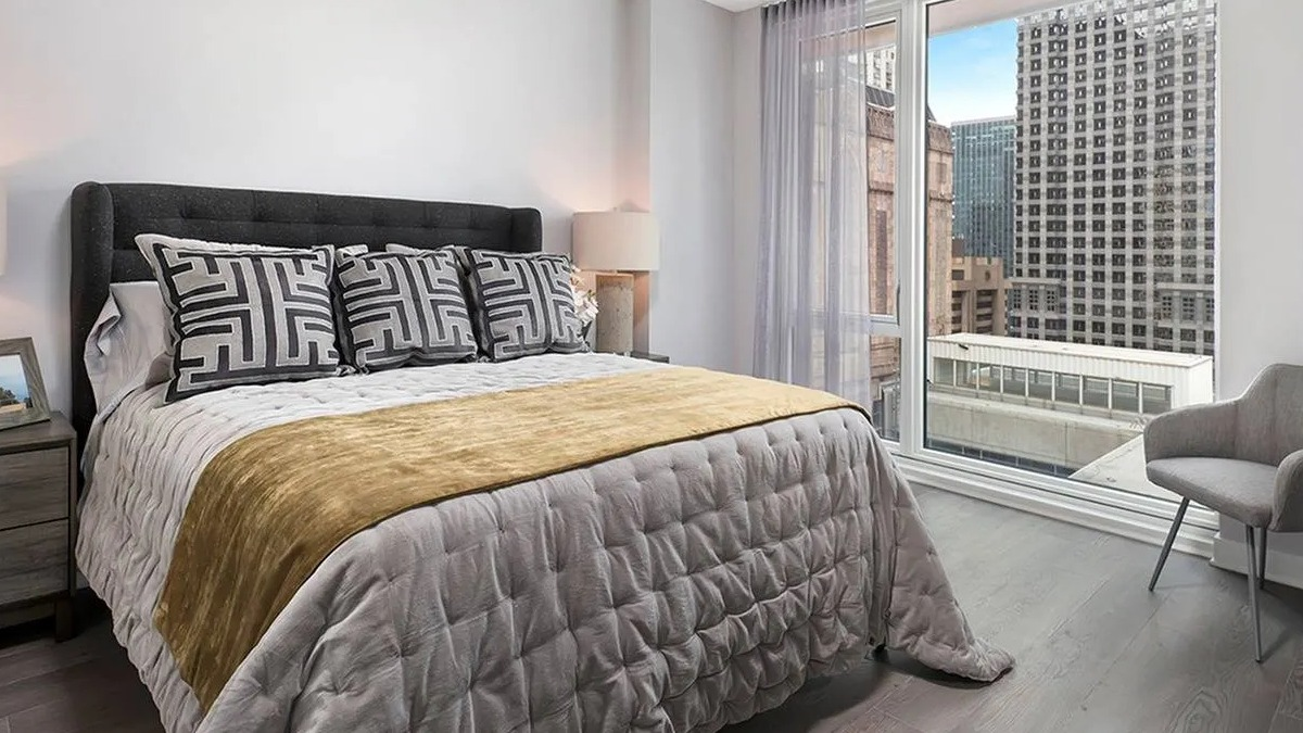 Contemporary bedroom with a large bed, elegant grey and gold bedding, and city views from expansive windows at Marquee at Block 37 in Chicago