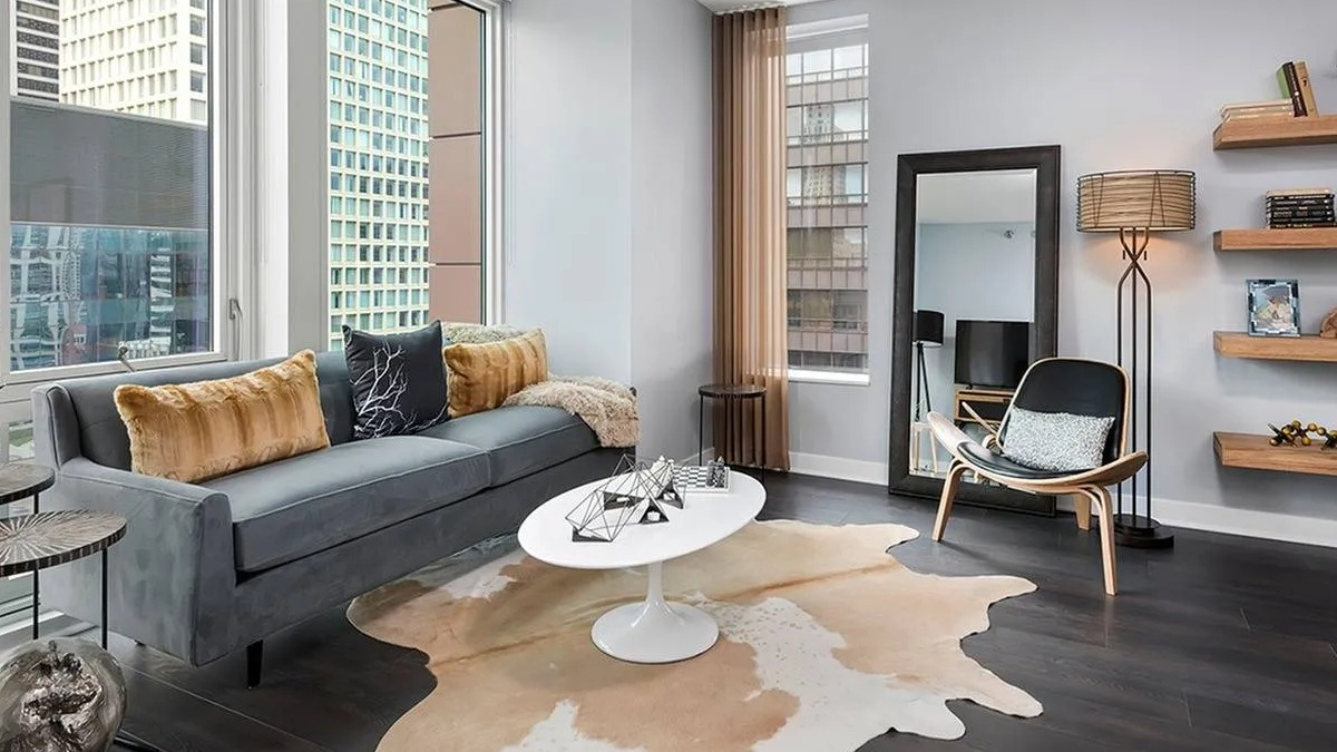 Spacious living room with a modern grey sofa, unique coffee table, and large windows offering city views at Marquee at Block 37 in Chicago