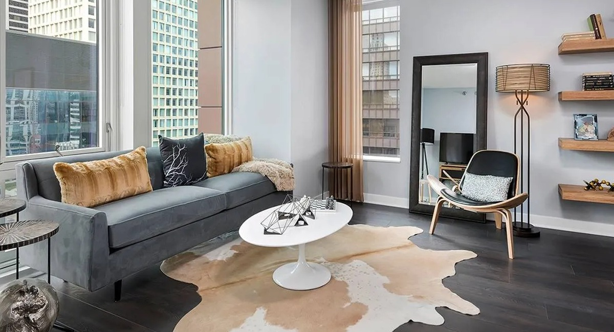Spacious living room with a modern grey sofa, unique coffee table, and large windows offering city views at Marquee at Block 37 in Chicago