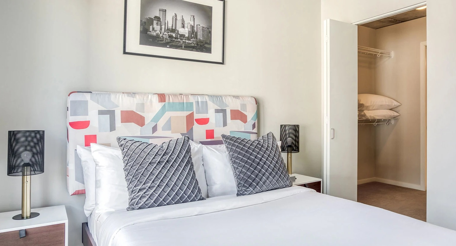 Contemporary bedroom with a patterned headboard, bedside tables, and an open closet showing shelving at MDA Apartments in Chicago