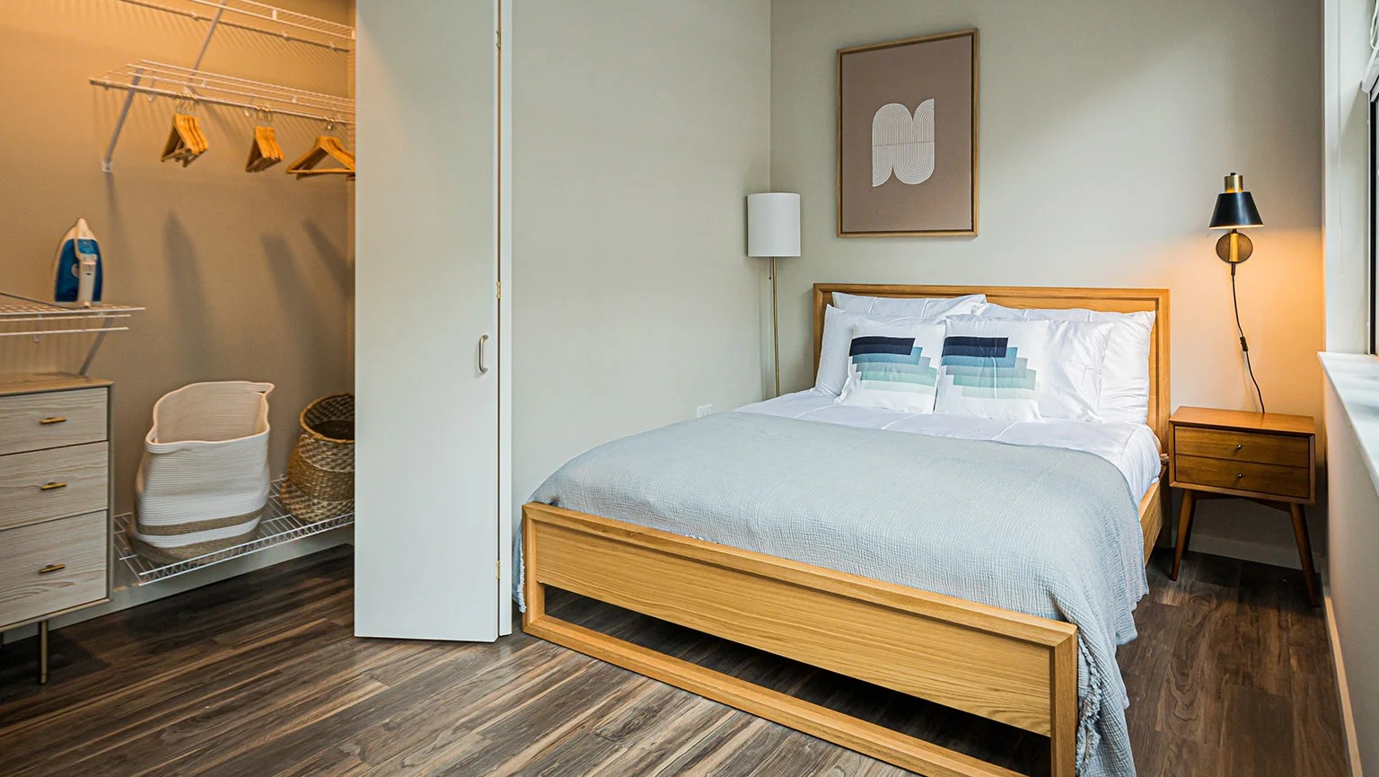 Modern bedroom with a wooden bed frame, stylish decor, and an open walk-in closet with shelving at MDA Apartments in Chicago
