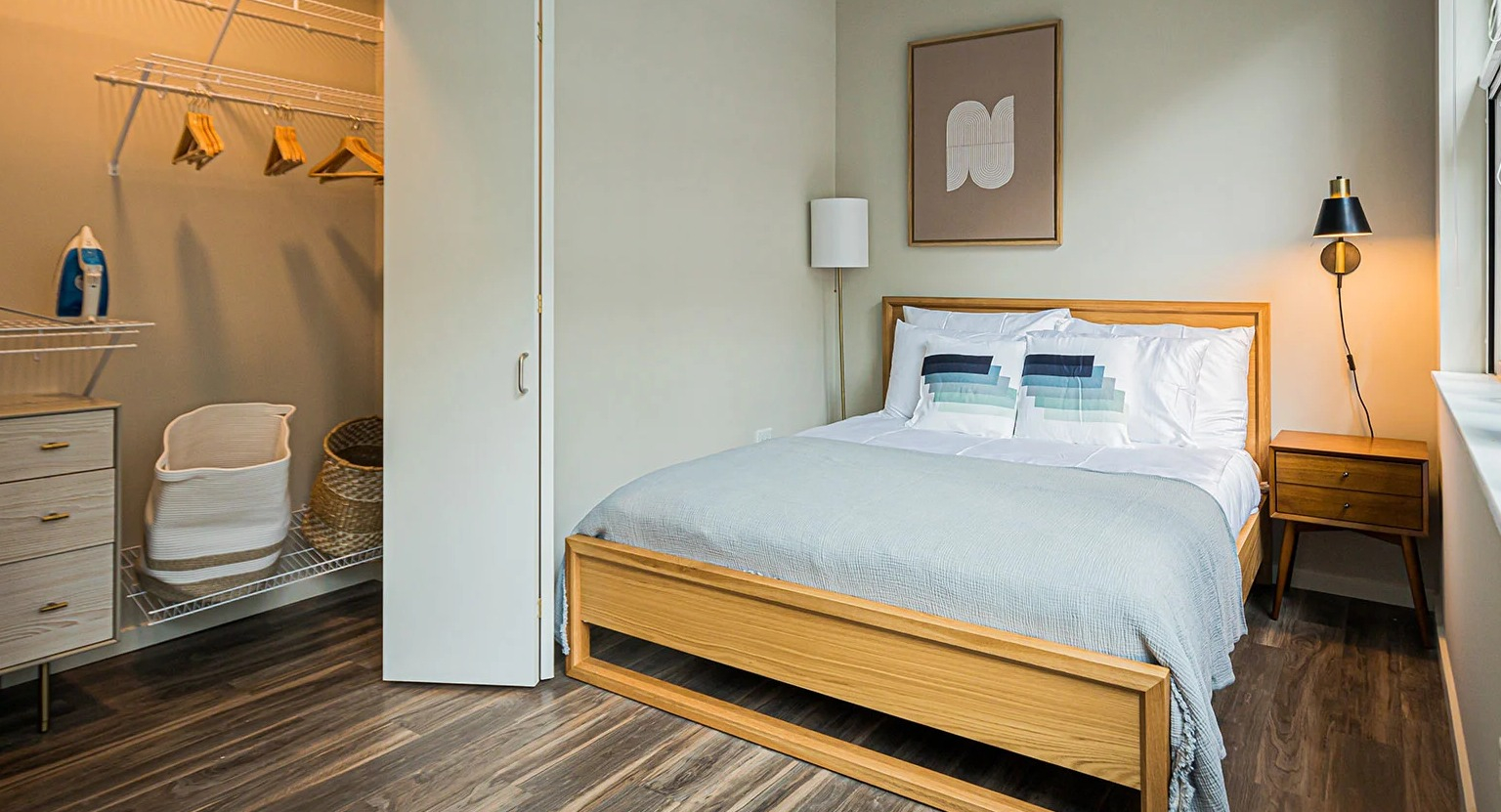 Modern bedroom with a wooden bed frame, stylish decor, and an open walk-in closet with shelving at MDA Apartments in Chicago