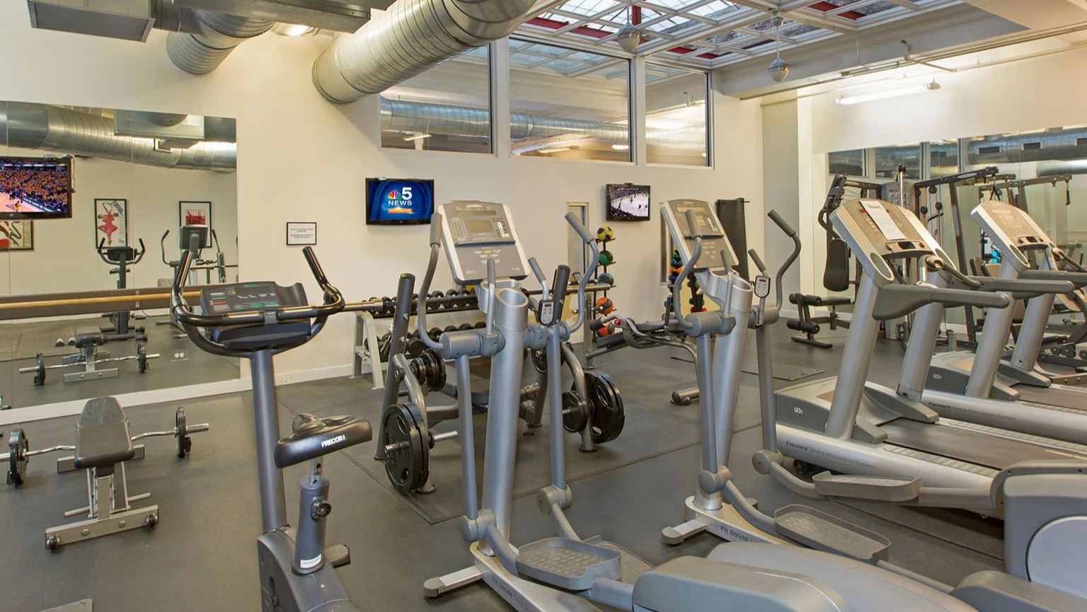 Well-equipped fitness center with various cardio machines, weight equipment, and TVs at MDA Apartments in Chicago