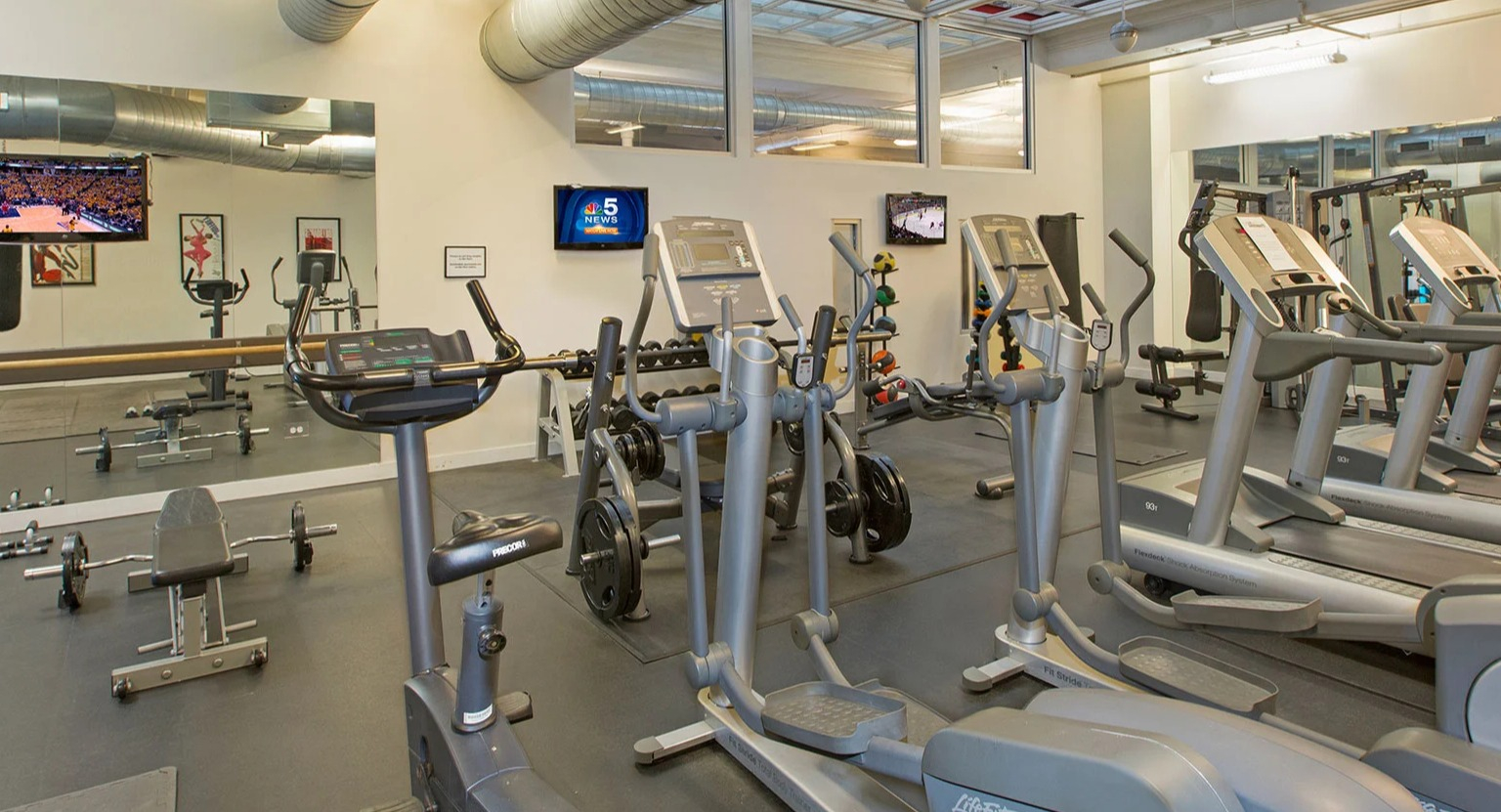 Well-equipped fitness center with various cardio machines, weight equipment, and TVs at MDA Apartments in Chicago