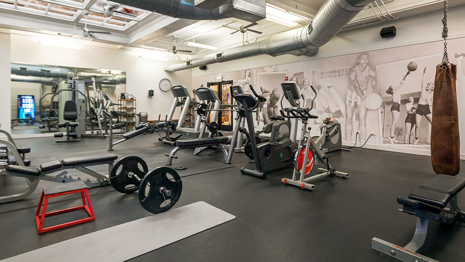 Spacious gym with free weights, weight benches, and a punching bag, featuring artistic wall murals at MDA Apartments in Chicago