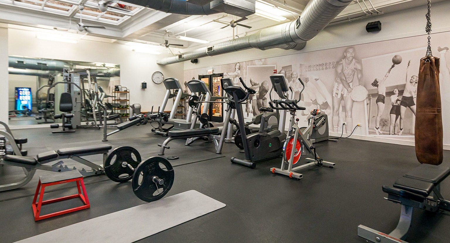Spacious gym with free weights, weight benches, and a punching bag, featuring artistic wall murals at MDA Apartments in Chicago