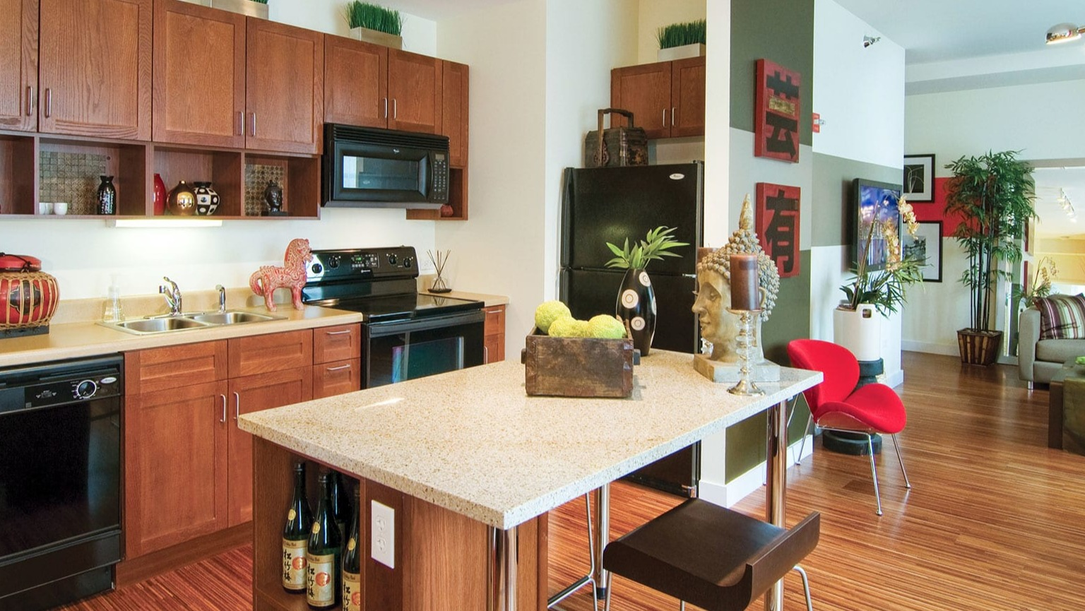 Open-concept kitchen with wood cabinets, black appliances, a central island, and a vibrant living area beyond at MDA Apartments in Chicago