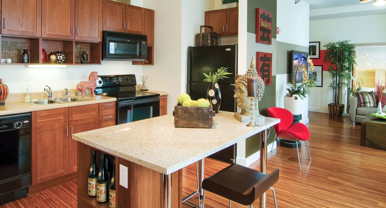 Open-concept kitchen with wood cabinets, black appliances, a central island, and a vibrant living area beyond at MDA Apartments in Chicago