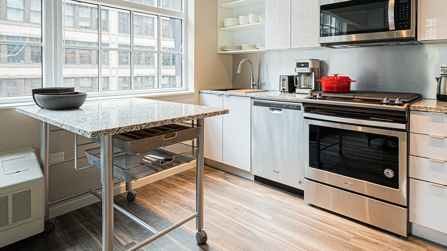 Modern kitchen with white cabinets, stainless steel appliances, and a movable island, bathed in natural light at MDA Apartments in Chicago