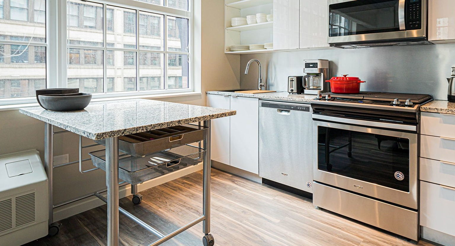Modern kitchen with white cabinets, stainless steel appliances, and a movable island, bathed in natural light at MDA Apartments in Chicago