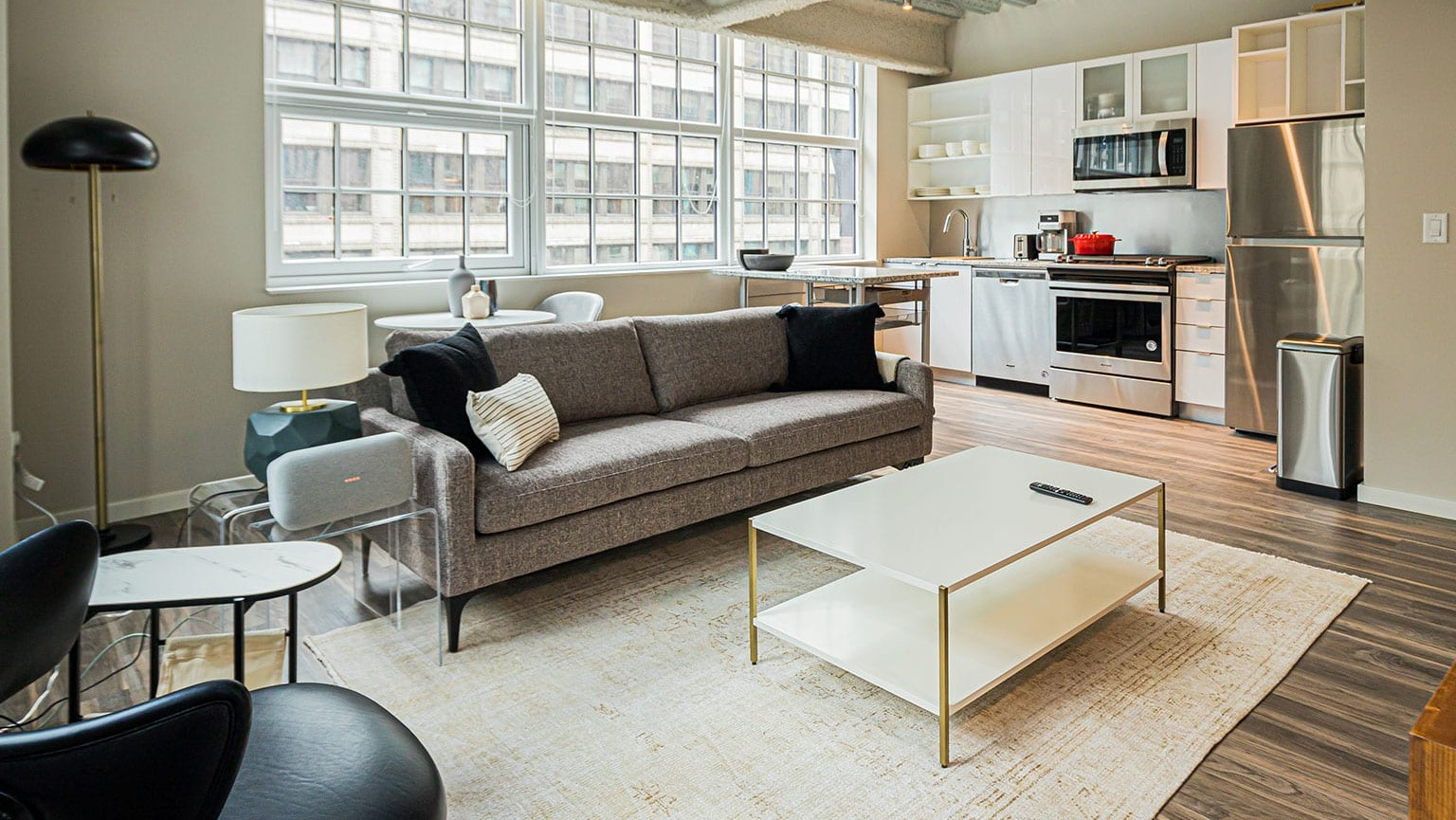 Open-concept loft-style living room and kitchen with high ceilings, large windows, and modern appliances at MDA Apartments in Chicago