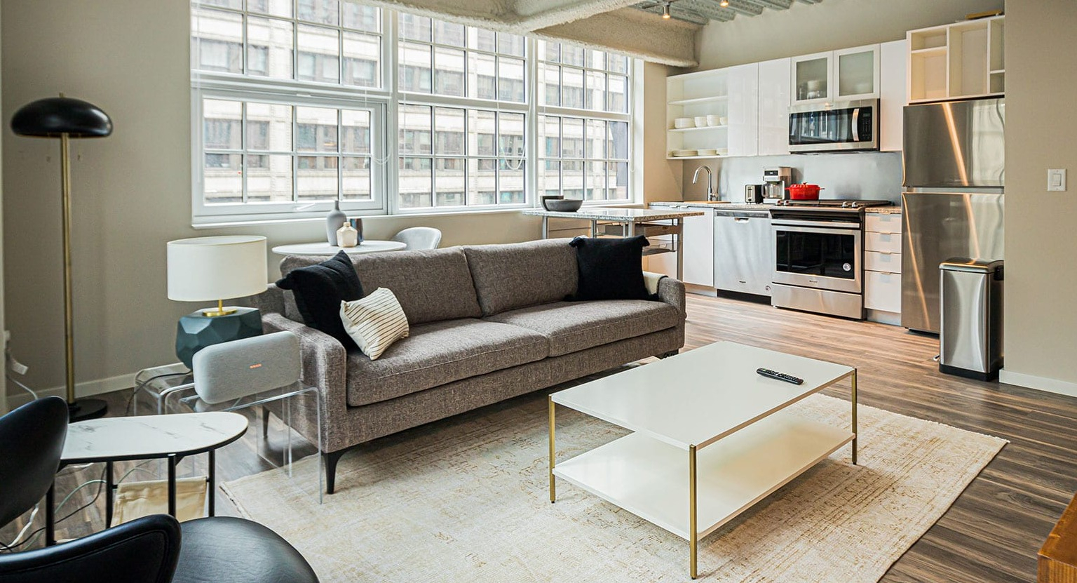Open-concept loft-style living room and kitchen with high ceilings, large windows, and modern appliances at MDA Apartments in Chicago