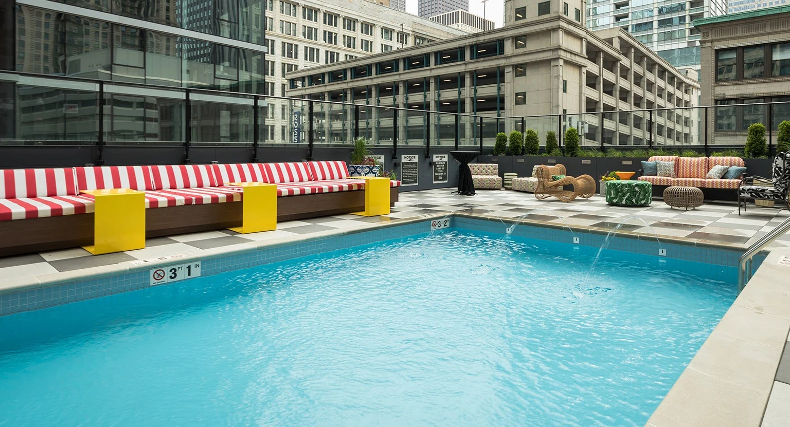 Inviting outdoor swimming pool surrounded by comfortable lounge seating and city buildings at MDA Apartments in Chicago