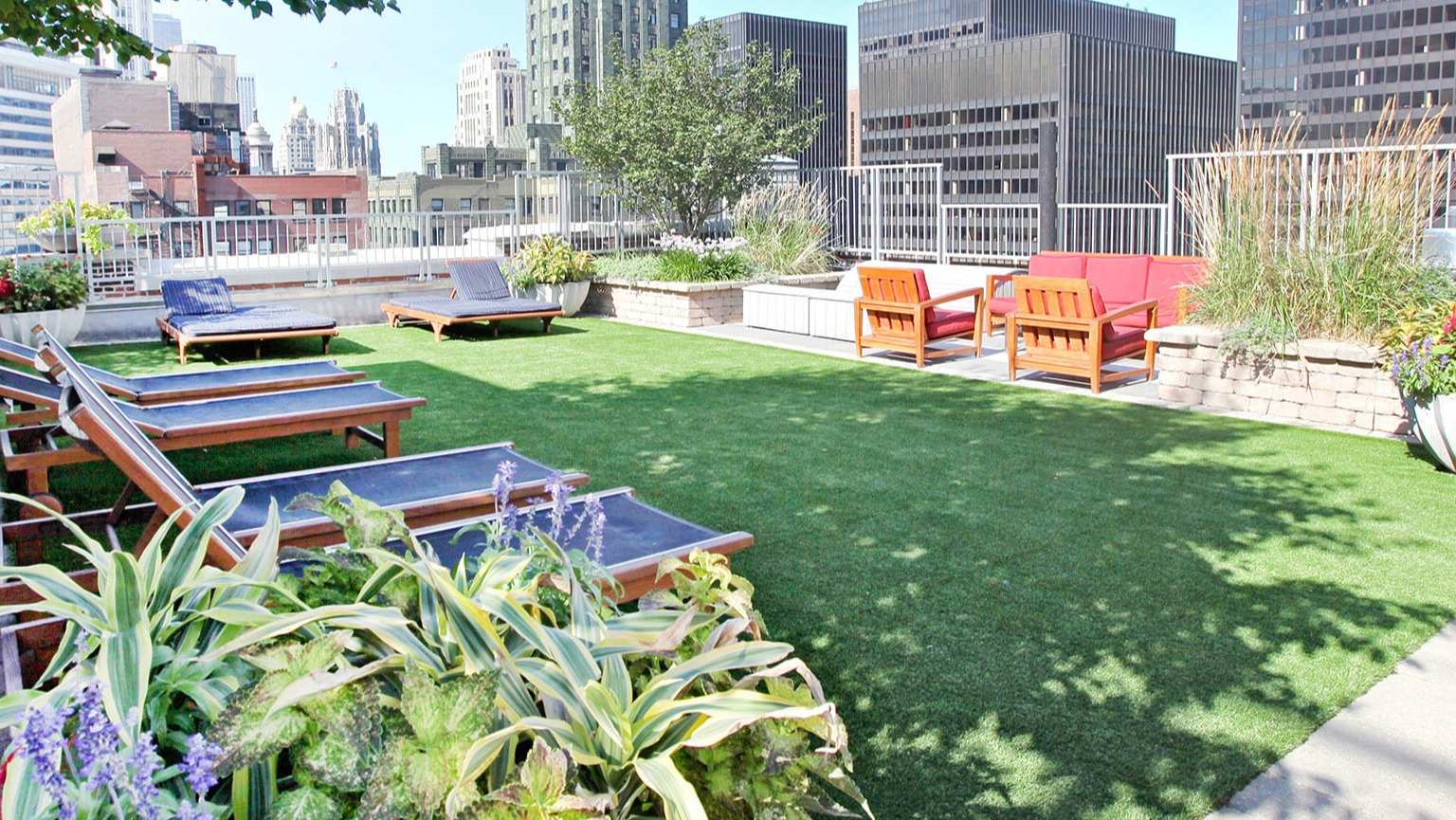 Lush rooftop deck with lounge chairs, green lawn, and city skyline views at MDA Apartments in Chicago