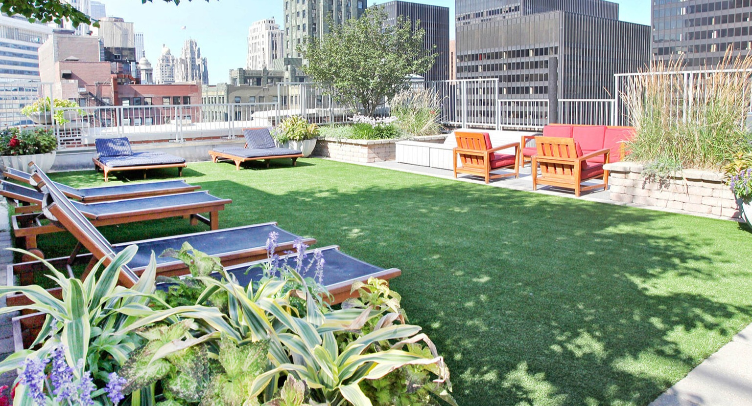 Lush rooftop deck with lounge chairs, green lawn, and city skyline views at MDA Apartments in Chicago