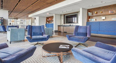Elegant clubroom lounge area with plush blue armchairs, stylish decor, and a large TV for entertainment at MILA Luxury Apartments in Chicago