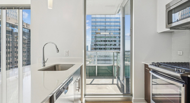 Sleek kitchen with white countertops, stainless steel appliances, and a door leading to a private balcony at MILA Luxury Apartments in Chicago
