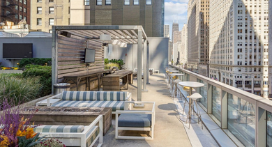 Modern outdoor terrace with comfortable seating, a grilling station, and a cozy fire pit, all with city views at MILA Luxury Apartments in Chicago